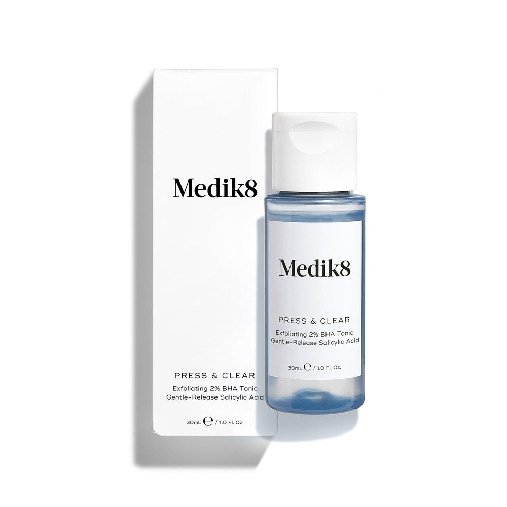 Medik8 Press & Glow tonic bottle stands in front of its matching white product carton on a clean white background. Text on both identifies the product as a travel sized Daily Exfoliating PHA Tonic with Enzyme Activator. 