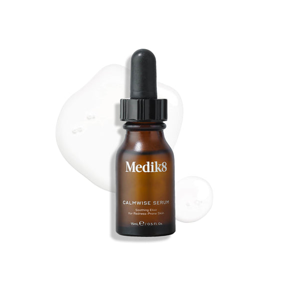 A brown glass dropper bottle of Calmwise Serum stands upright on a white surface, surrounded by clear serum droplets. -18
