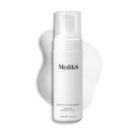 A Medik8 Gentle Cleanse pump bottle displayed on a white background with a smear of white foam behind it, highlighting the product's hydrating texture.