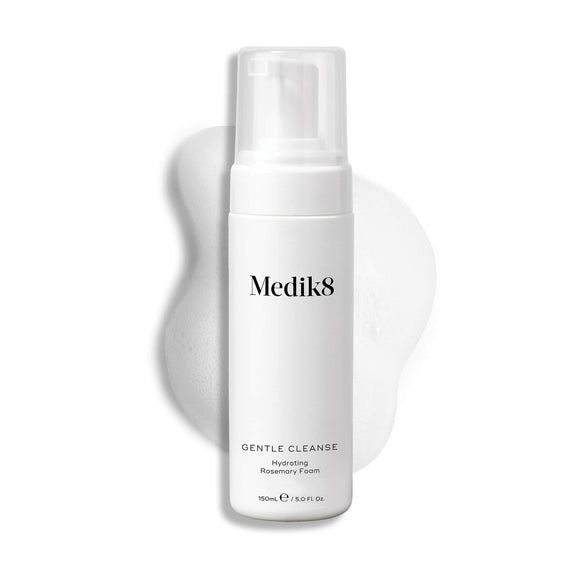 A Medik8 Gentle Cleanse pump bottle displayed on a white background with a smear of white foam behind it, highlighting the product's hydrating texture.-6