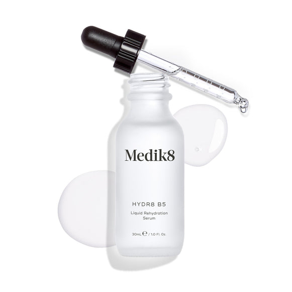 Medik8 Hydr8 B5 serum bottle stands against a clean white background with a clear liquid puddle and droplets, with the dropper resting on top. Text identifies the product as a 30mL  Liquid Rehydration Serum. -24