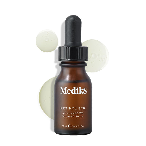 Medik8 Retinol 3TR serum bottle displayed against a clean white background with translucent serum droplets. The amber glass bottle with a black dropper cap features the Medik8 logo and is labeled  RETINOL 3TR Advanced 0.3% Vitamin A Serum  in a 15mL size.
