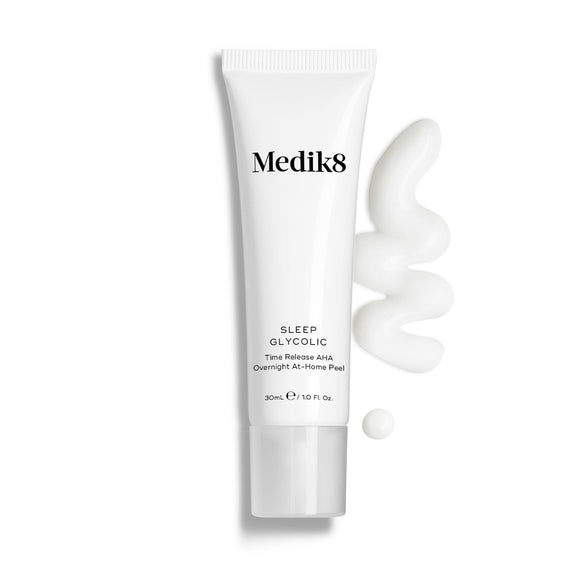 Medik8 Sleep Glycolic tube stands against a clean white background with a wavy swipe and a small droplet of white cream texture. Text identifies the product as a Time Release AHA Overnight At-Home Peel in a 30mL size.-10