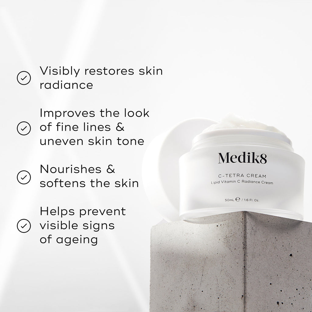 Medik8 C-Tetra Cream jar displayed on a grey stone block against a white background with soft light rays. The image features four check-marked claims:

Visibly restores skin radiance

Improves the look of fine lines & uneven skin tone

Nourishes & softens the skin

Helps prevent visible signs of ageing