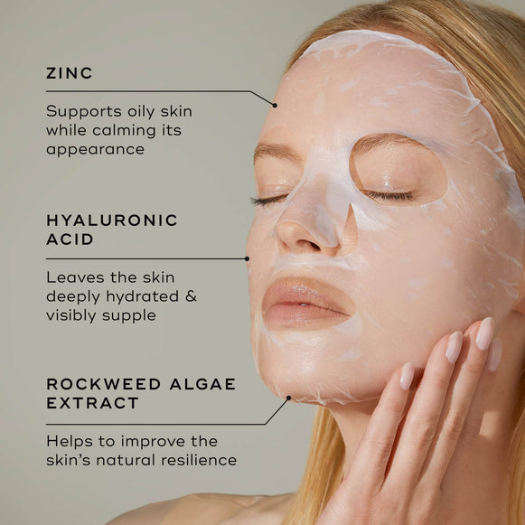 Close-up of a person wearing a translucent white sheet mask on their face against a light grey background. Text points to key ingredients: ZINC (Supports oily skin while calming its appearance), HYALURONIC ACID (Leaves the skin deeply hydrated & visibly supple), and ROCKWEED ALGAE EXTRACT (Helps to improve the skin's natural resilience).-hover-33