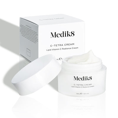 Medik8 C-Tetra Cream jar and its white cardboard carton displayed on a clean white background with soft shadows. The open white, frosted-glass jar features the Medik8 logo and is labeled  C-TETRA CREAM Lipid Vitamin C Radiance Cream  in a 50mL size. A thick swirl of white cream is visible on top of the jar, with the white box behind it showing the product name and a partial ingredients list.