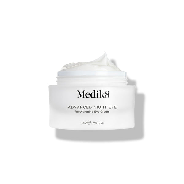 Medik8 Advanced Night Eye cream jar stands against a white background with the lid removed. The rich white cream is visible inside the jar, highlighting its texture.