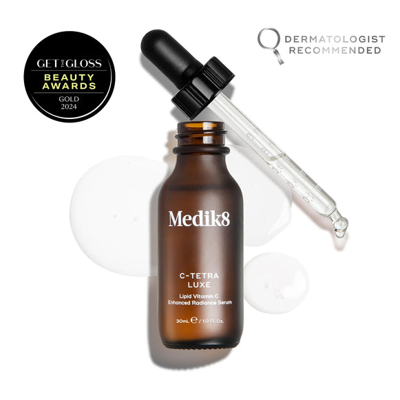 Medik8 C-Tetra Luxe serum bottle shown open with its glass pipette resting against the rim, displayed on a white background with clear, translucent serum droplets. The image includes a  GET THE GLOSS BEAUTY AWARDS GOLD 2024  seal in the top left and a  DERMATOLOGIST RECOMMENDED  emblem with a magnifying glass icon in the top right.-9