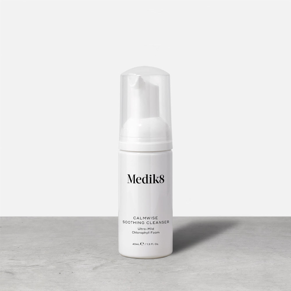 A travel-size pump bottle (40ml) of Medik8 Calmwise Soothing Cleanser displayed on a grey surface. Text describes it as an  Ultra-Mild Chlorophyll Foam. 