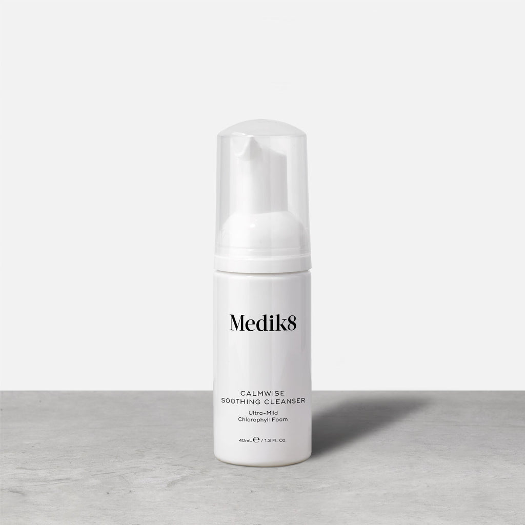A travel-size pump bottle (40ml) of Medik8 Calmwise Soothing Cleanser displayed on a grey surface. Text describes it as an  Ultra-Mild Chlorophyll Foam. 