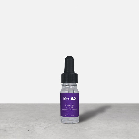A purple 8ml glass dropper bottle of Medik8 HYDR8 B5 INTENSE serum stands next to its white packaging box on a grey surface against a white background. Text on both reads: "Medik8, HYDR8 B5 INTENSE, Hyaluronic Acid with NMF Replenish & Boost, 8mLe / 0.27 Fl. Oz.".-20