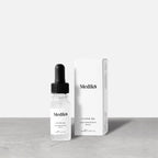 Medik8 Hydr8 B5 travel-sized serum bottle stands next to its matching white product carton on a grey textured surface against a neutral background. Text on the 8mL bottle identifies it as a ""Liquid Rehydration Serum."""