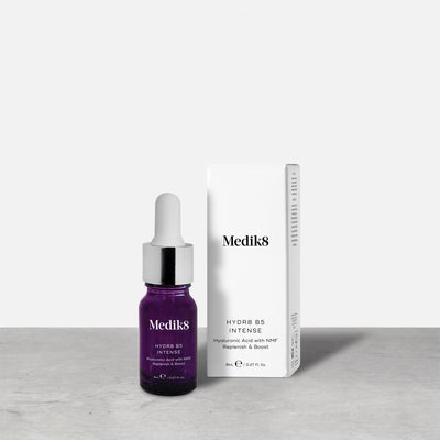 A purple 8ml glass dropper bottle of Medik8 HYDR8 B5 INTENSE serum stands next to its white packaging box on a grey surface against a white background. Text on both reads: "Medik8, HYDR8 B5 INTENSE, Hyaluronic Acid with NMF Replenish & Boost, 8mLe / 0.27 Fl. Oz.".