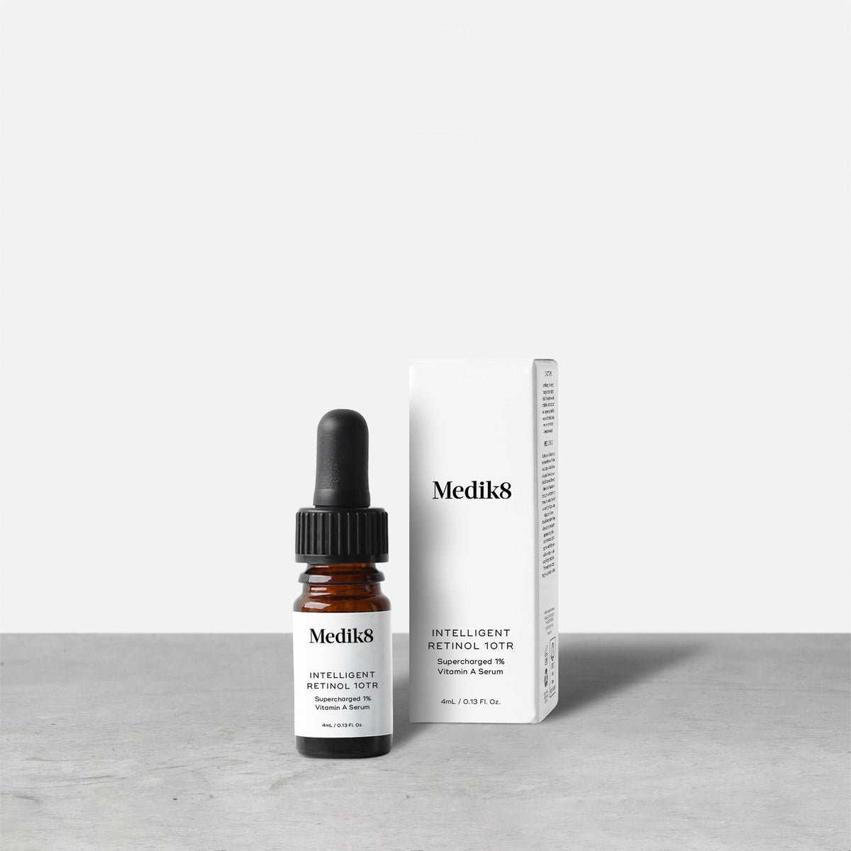 Medik8 Intelligent Retinol 10TR serum bottle stands next to its matching white product carton on a grey textured surface against a neutral background. Text on the 4mL bottle identifies it as a  Supercharged 1% Vitamin A Serum. 