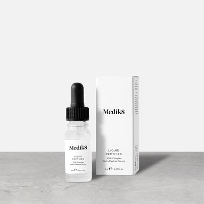 A small clear glass bottle (8mL) of Medik8 Liquid Peptides serum, with its dropper resting beside it. Text indicates it's  ALSO AVAILABLE IN A HANDY TRAVEL SIZE.