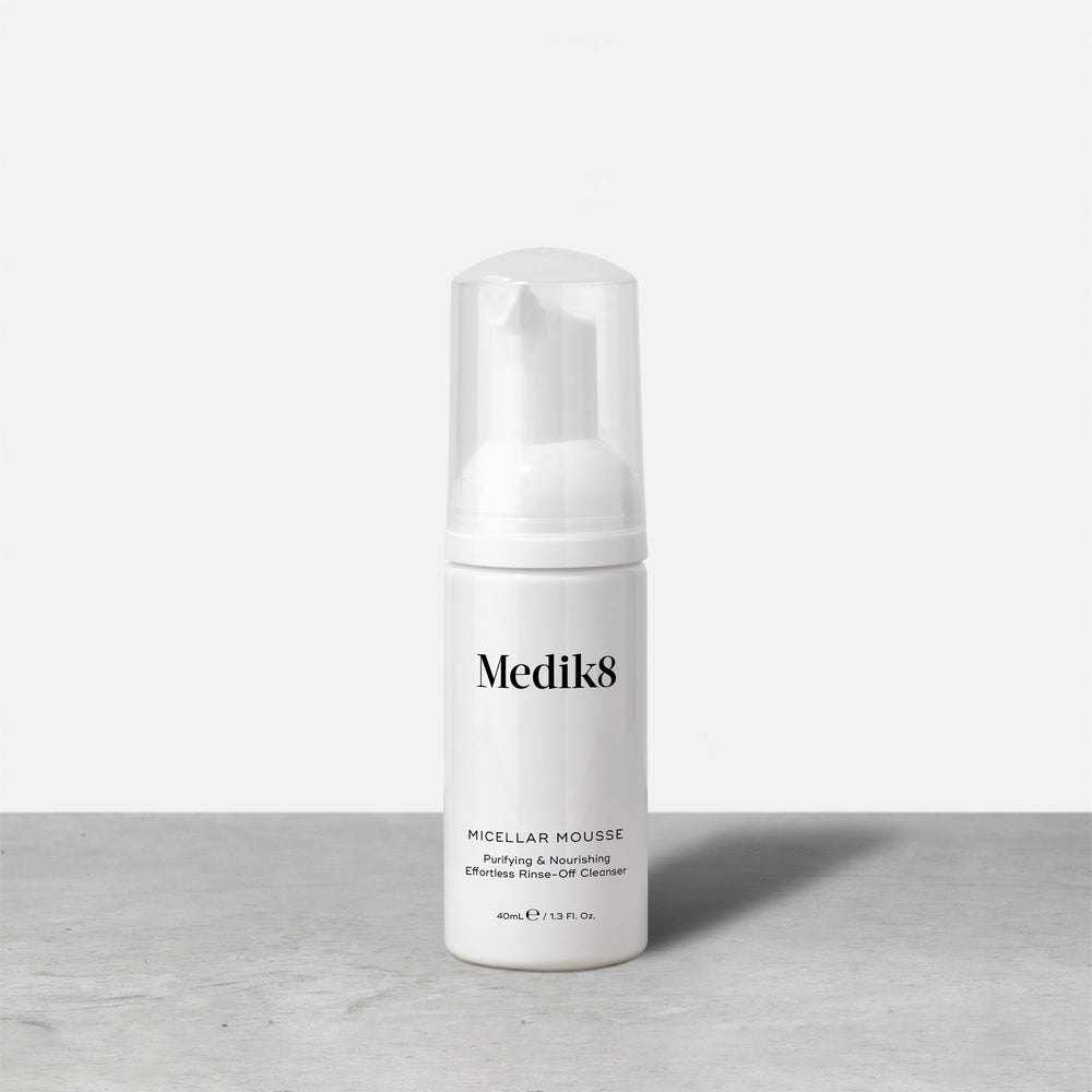 A travel-size pump bottle (40ml) of Medik8 Micellar Mousse displayed on a grey surface. Text describes it as a  Purifying & Nourishing Effortless Rinse-Off Cleanser. 