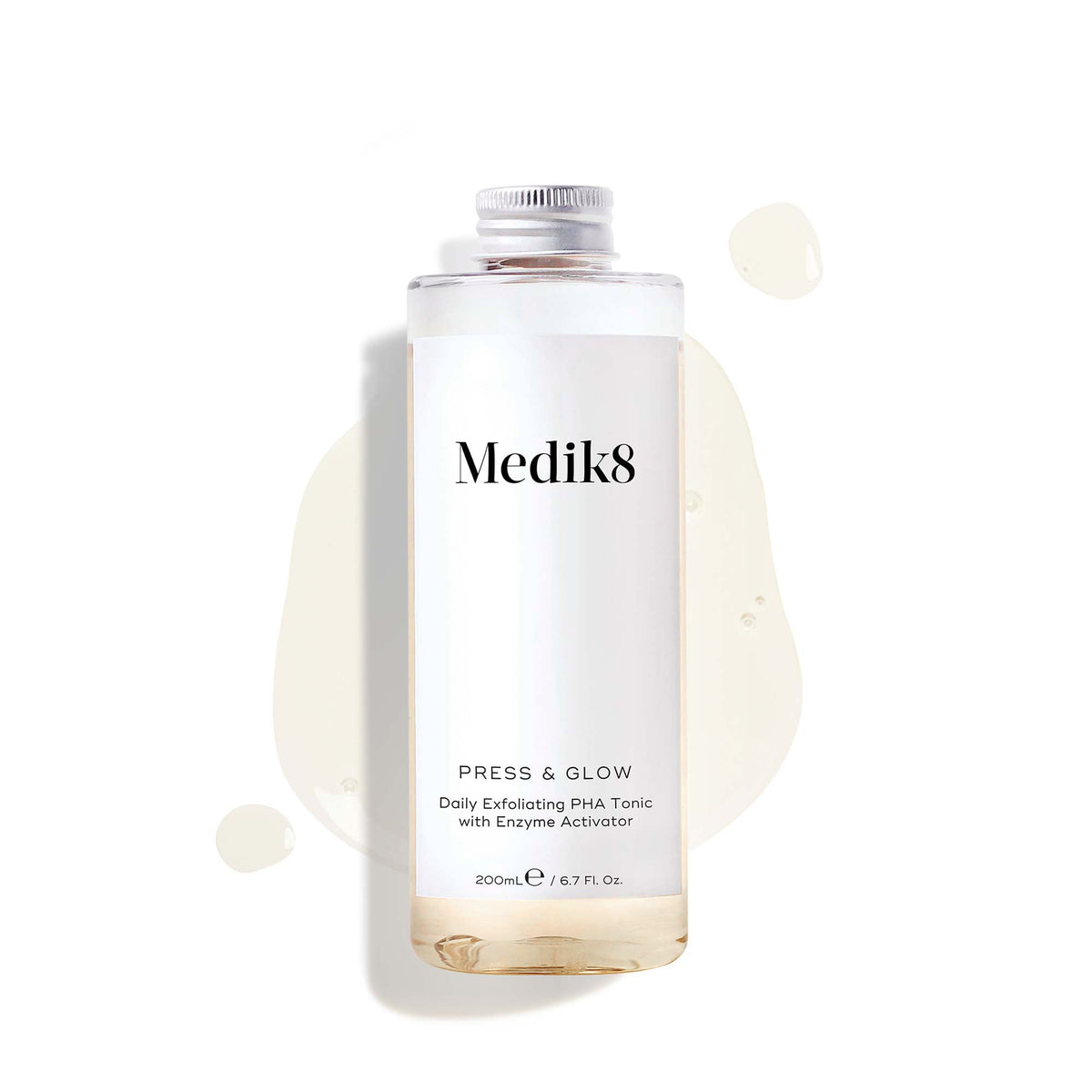 A 200mL clear refill bottle of Medik8 Press & Glow exfoliating tonic featuring a silver screw cap. Set against a white background, the bottle sits amidst a puddle and droplets of the pale yellow tonic, showcasing its liquid texture. The label text reads ""Daily Exfoliating PHA Tonic with Enzyme Activator."