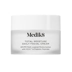 A travel-sized 12.5mL frosted jar of Medik8 Total Moisture Daily Facial Cream standing next to its white cardboard carton. The products are displayed on a textured grey surface against a clean white background. Text on both reads: "AM/PM Multi-Layered Moisturisation with H.E.O.™ & Prebiotic Peptides."