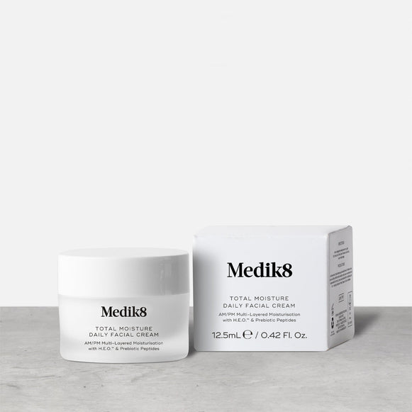 A travel-sized 12.5mL frosted jar of Medik8 Total Moisture Daily Facial Cream standing next to its white cardboard carton. The products are displayed on a textured grey surface against a clean white background. Text on both reads: "AM/PM Multi-Layered Moisturisation with H.E.O.™ & Prebiotic Peptides."-20